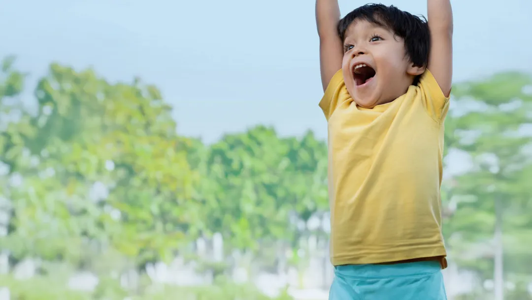a boy raises his arms and laughs outdoor