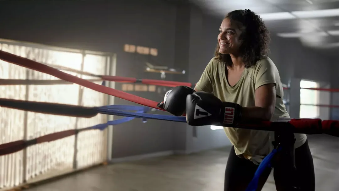 female boxer smiling while resting on the ropes