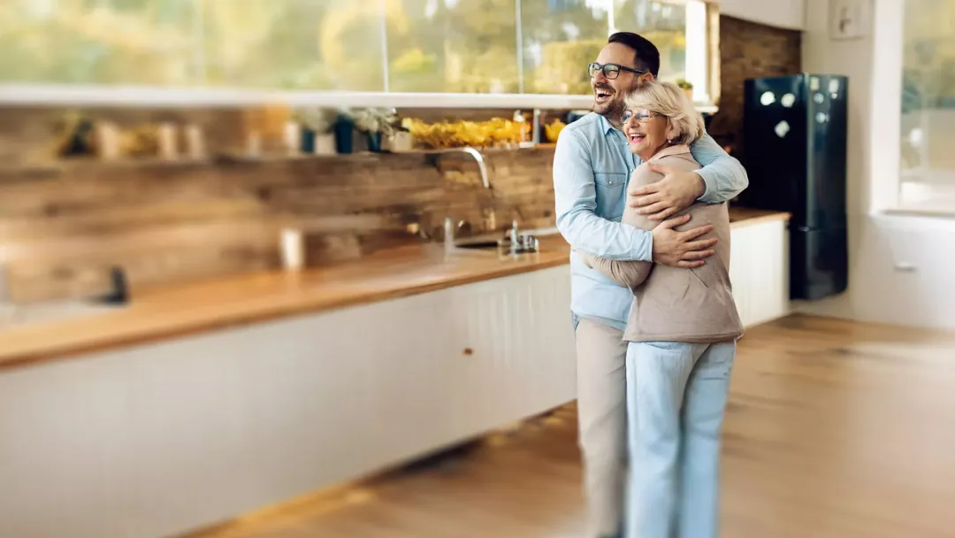 man hugging his mother and laughing indoors