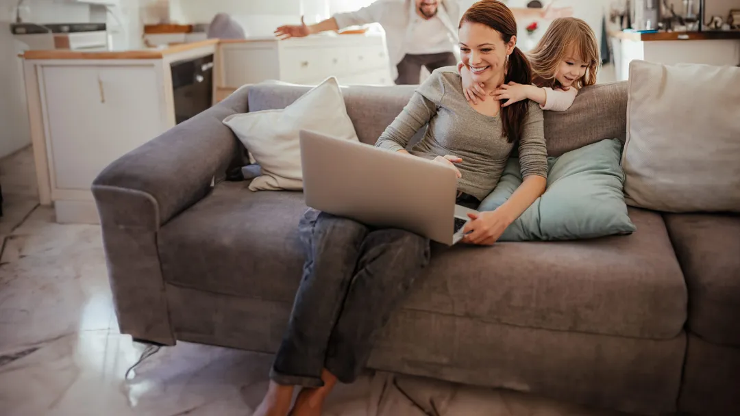 daughter-hugs-her-mom-as-she-looks-at-a-laptop