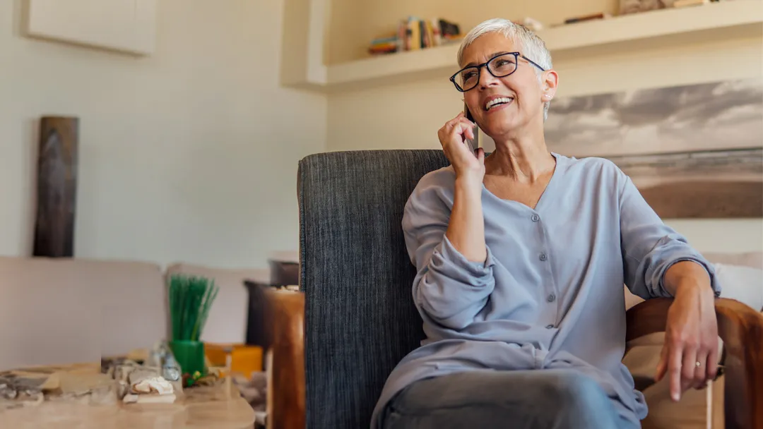 Senior woman smiling while talking on the phone while sitting at home.