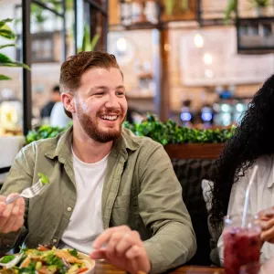 A young man eating health food a table with friends.