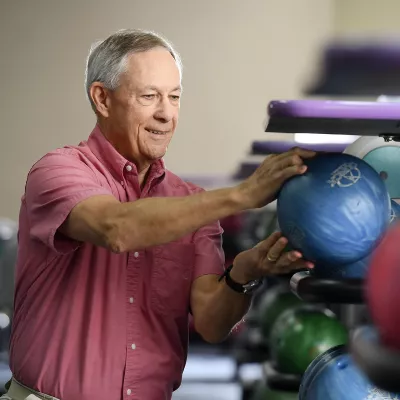 An adult man crouches to choose a bowling ball at the bowling alley.