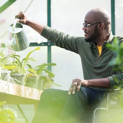 Bearded man in wheelchair watering plants