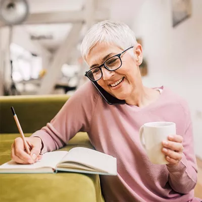 Elder woman writing and drinking with mug