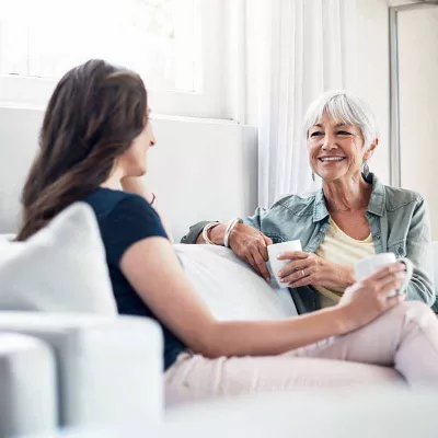 Elderly woman with adult daughter on couch, drinking coffee