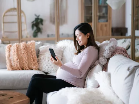 Pregnant woman sitting on couch with phone smiling