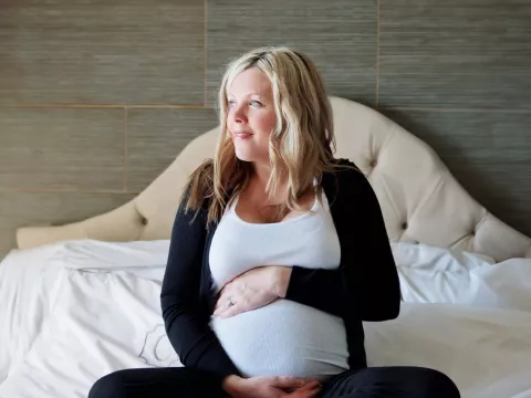 Pregnant woman sitting on bed holding belly