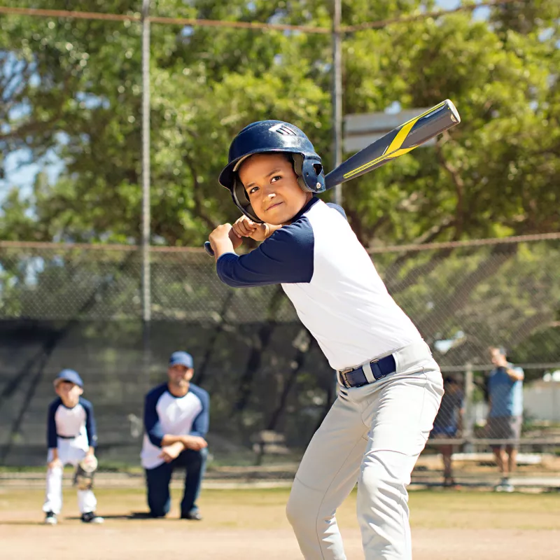 A boy playing baseball in the park with his father and his brother.