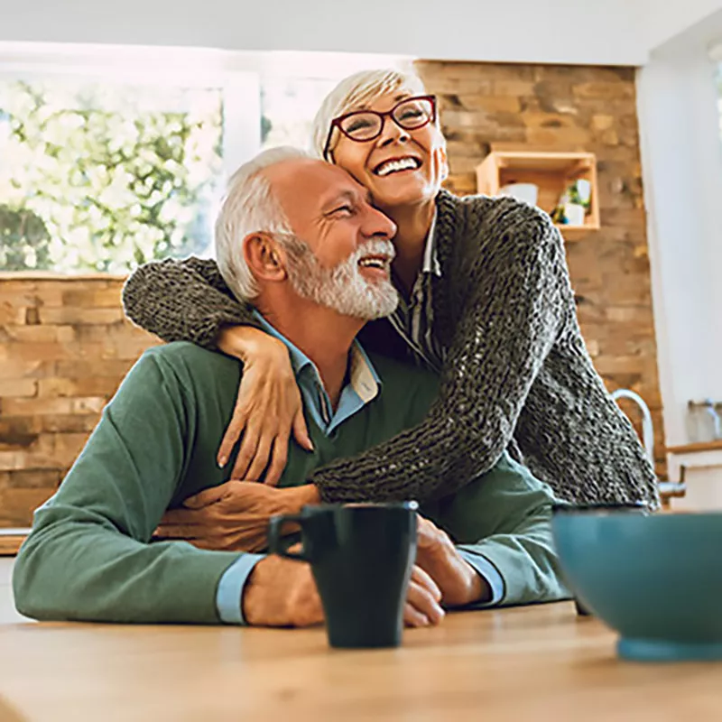 older-couple-hugging-and-laughing-indoors