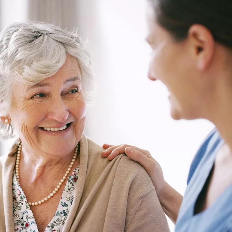 Female nurse in blue smiling at older woman