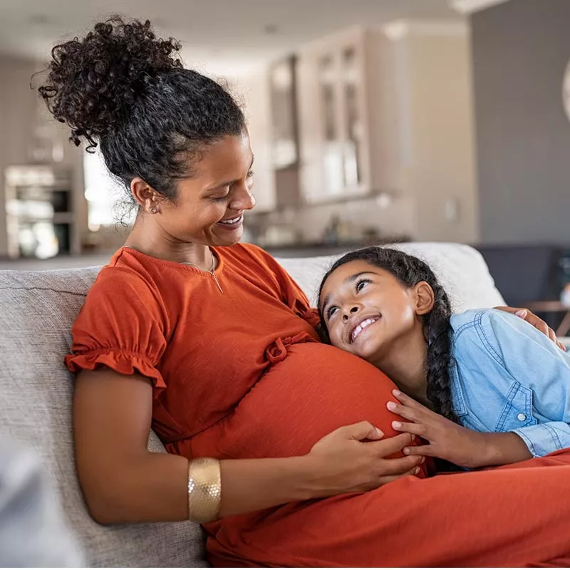 Pregnant woman smiling and daughter on couch