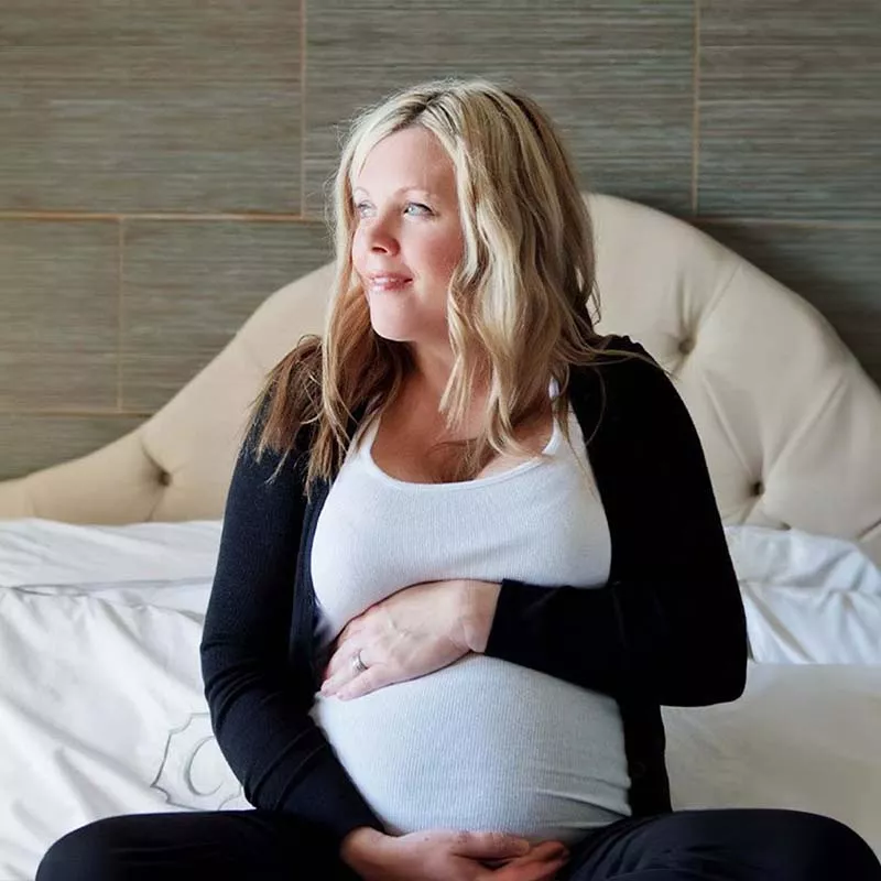 Pregnant woman sitting on bed holding belly