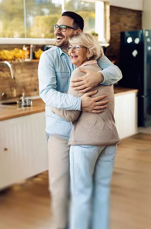 man hugging his mother and laughing indoors