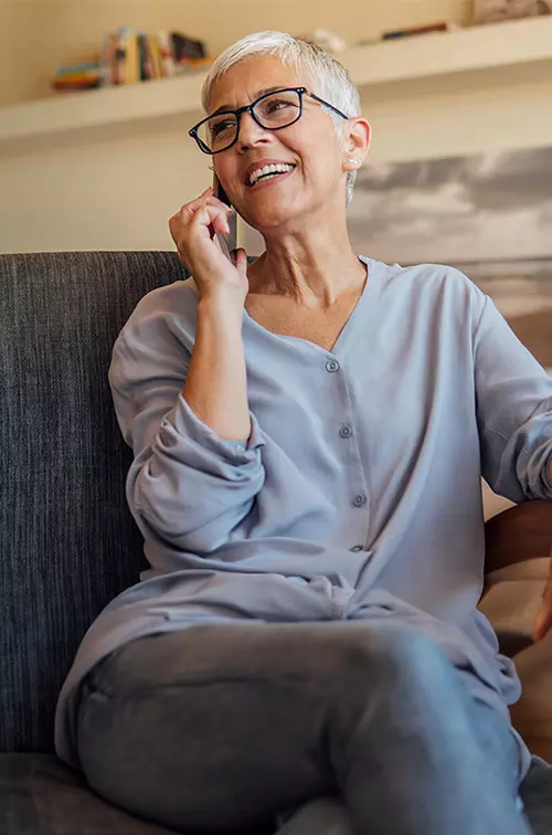 Senior woman smiling while talking on the phone while sitting at home.